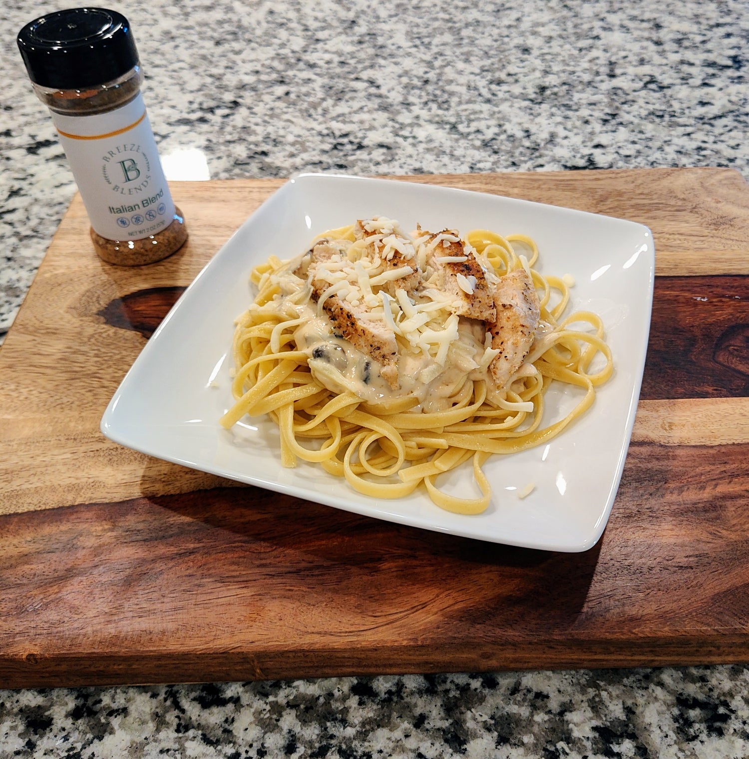 Chicken fettuccini alfredo on brown cutting board with shaker bottle
