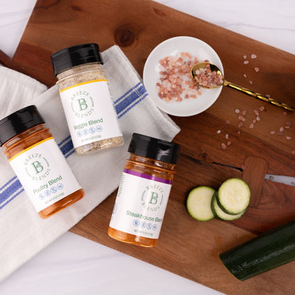 Breeze Blends seasoning bottles on a wooden cutting board with zucchini and salt.
