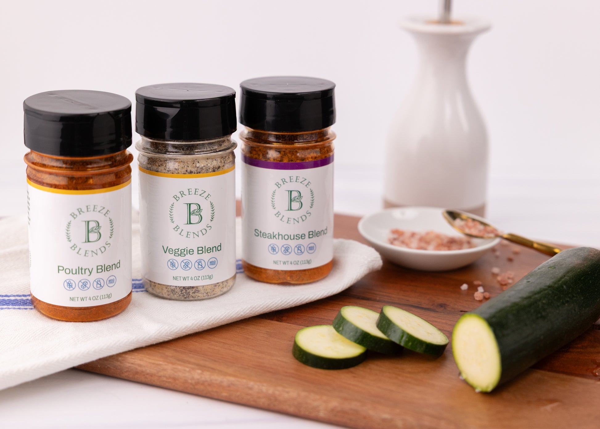 Breeze Blends BBQ Pack of three seasoning blends on a white kitchen towel with zucchini slices on a wooden board.