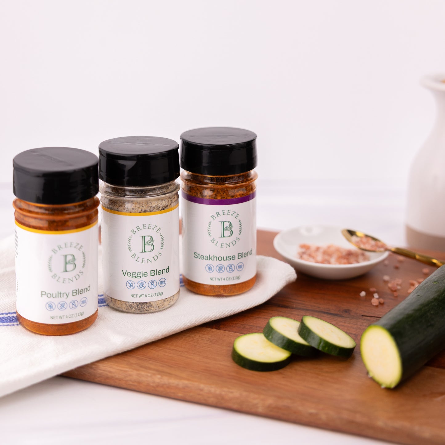Breeze Blends BBQ pack of three spice jars labeled 'Poultry Blend', 'Veggie Blend', and 'Steakhouse Blend' on a cutting board with zucchini slices.