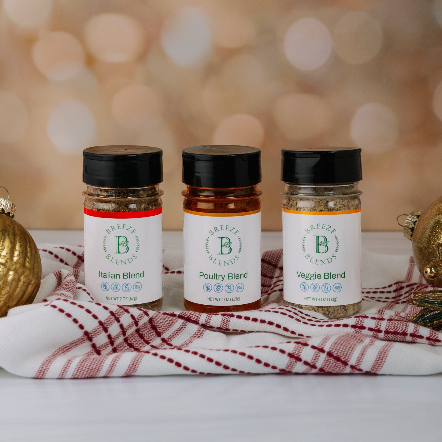 Breeze Blends thee spice jars labeled 'Italian Blend', 'Poultry Blend', and 'Veggie Blend' on a decorative cloth with a blurred background.