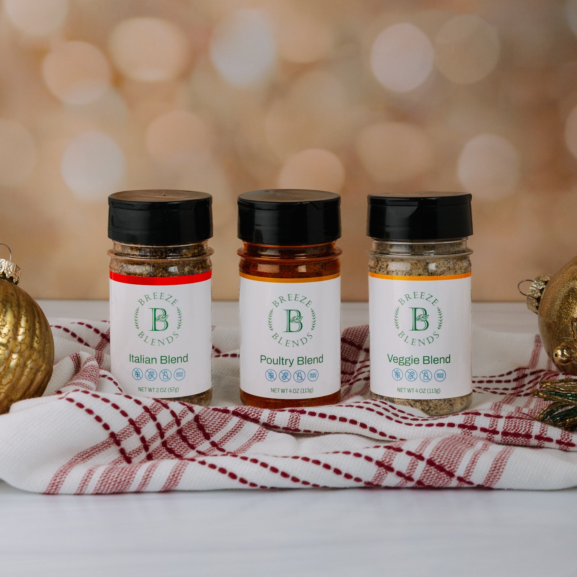 Breeze Blends thee spice jars labeled 'Italian Blend', 'Poultry Blend', and 'Veggie Blend' on a decorative cloth with a blurred background.