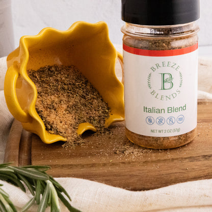 Bottle of Breeze Blends Italian Blend spice with a yellow bowl of spices on a wooden board.