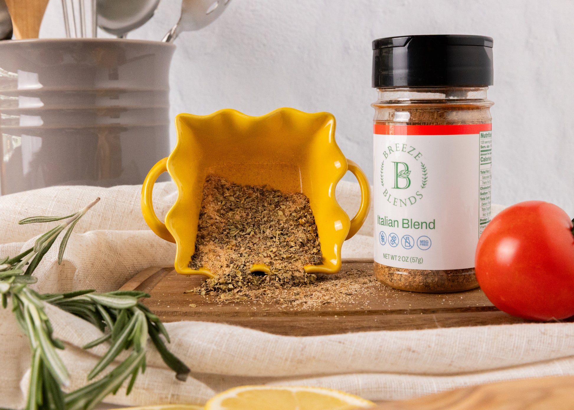 Breeze Blends Italian Blend in a yellow bowl on a wooden board, surrounded by herbs and a tomato.