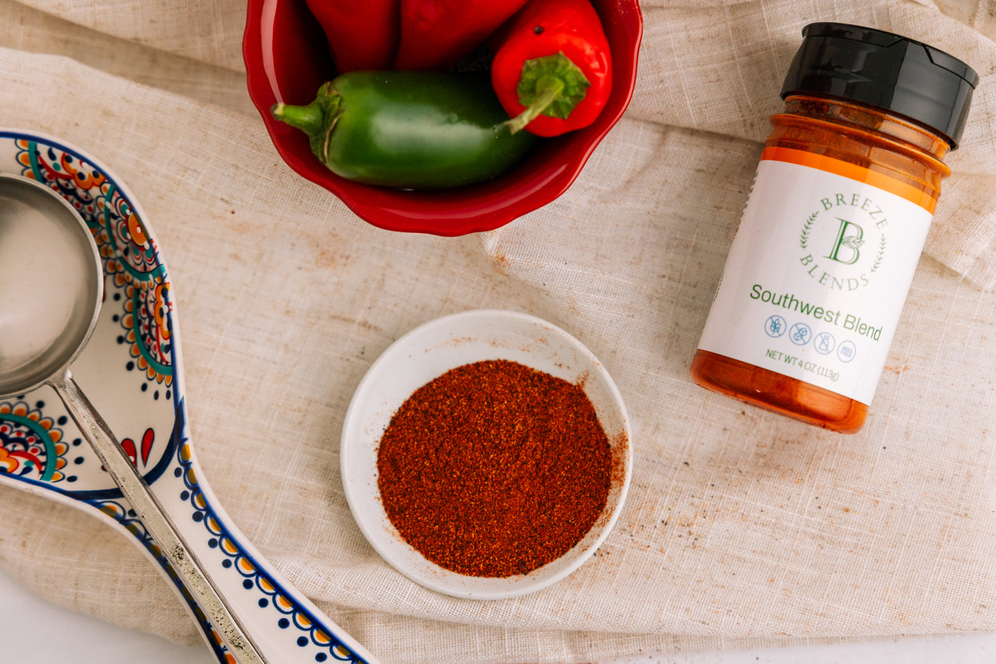 Bottle of Breeze Blends Southwest Blend in a small bowl with a bottle of seasoning and peppers on a textured surface