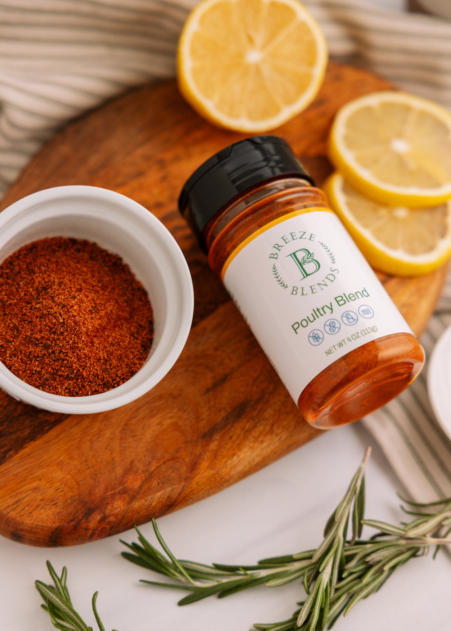 Bottle of Breeze Blends Poultry Blend on a wooden cutting board with lemons and spices