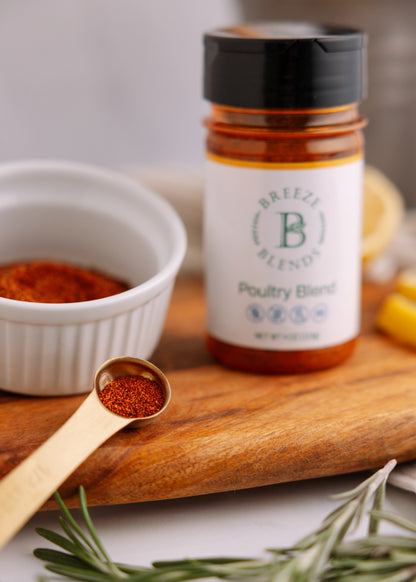 Bottle of Breeze Blend Poultry Blend on a wooden board with a spoonful of seasoning and rosemary.