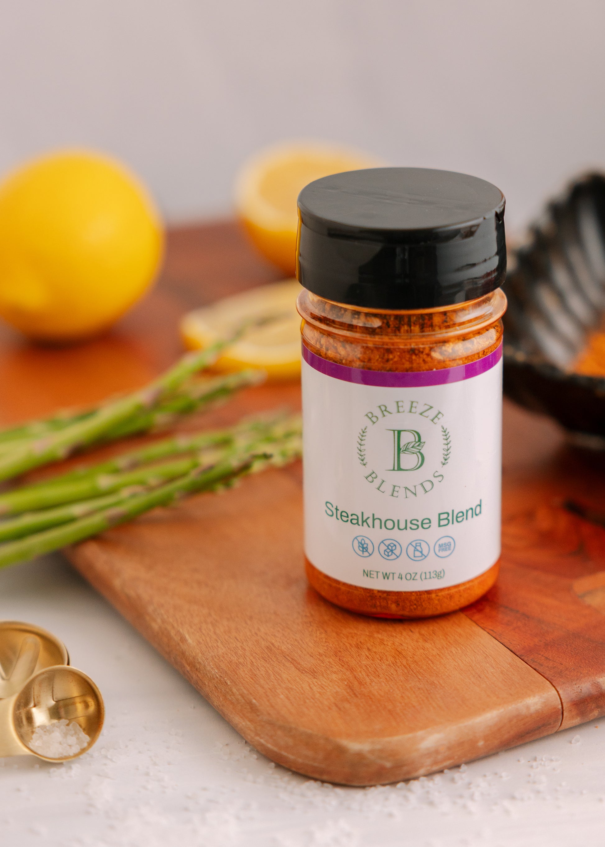 Breeze Blends Steakhouse Blend seasoning jar on a wooden cutting board with lemons and asparagus in the background.