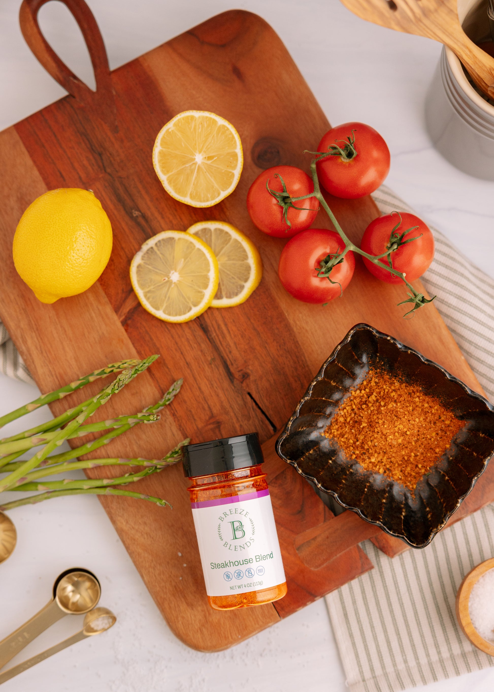 Wooden cutting board with lemons, tomatoes, and a bottle of Steakhouse seasoning on a white surface.