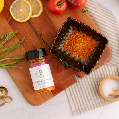Breeze Blends Steakhouse Blend seasoning on a wooden cutting board with lemons, tomatoes, and asparagus.